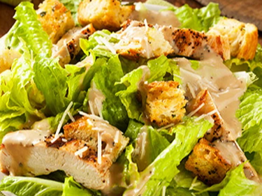 Ensalada César de pollo con lechuga, croutones, queso y aderezo César.